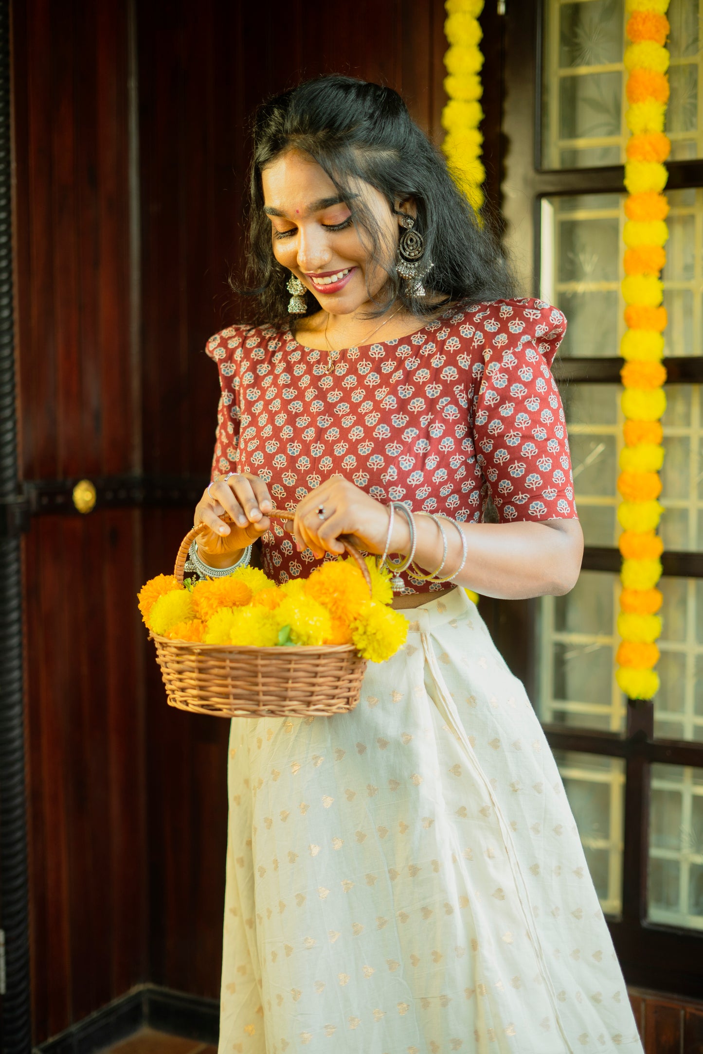 Women's red Ajrakh print crop top by Jacinda paired with a white skirt holding a basket of yellow flowers